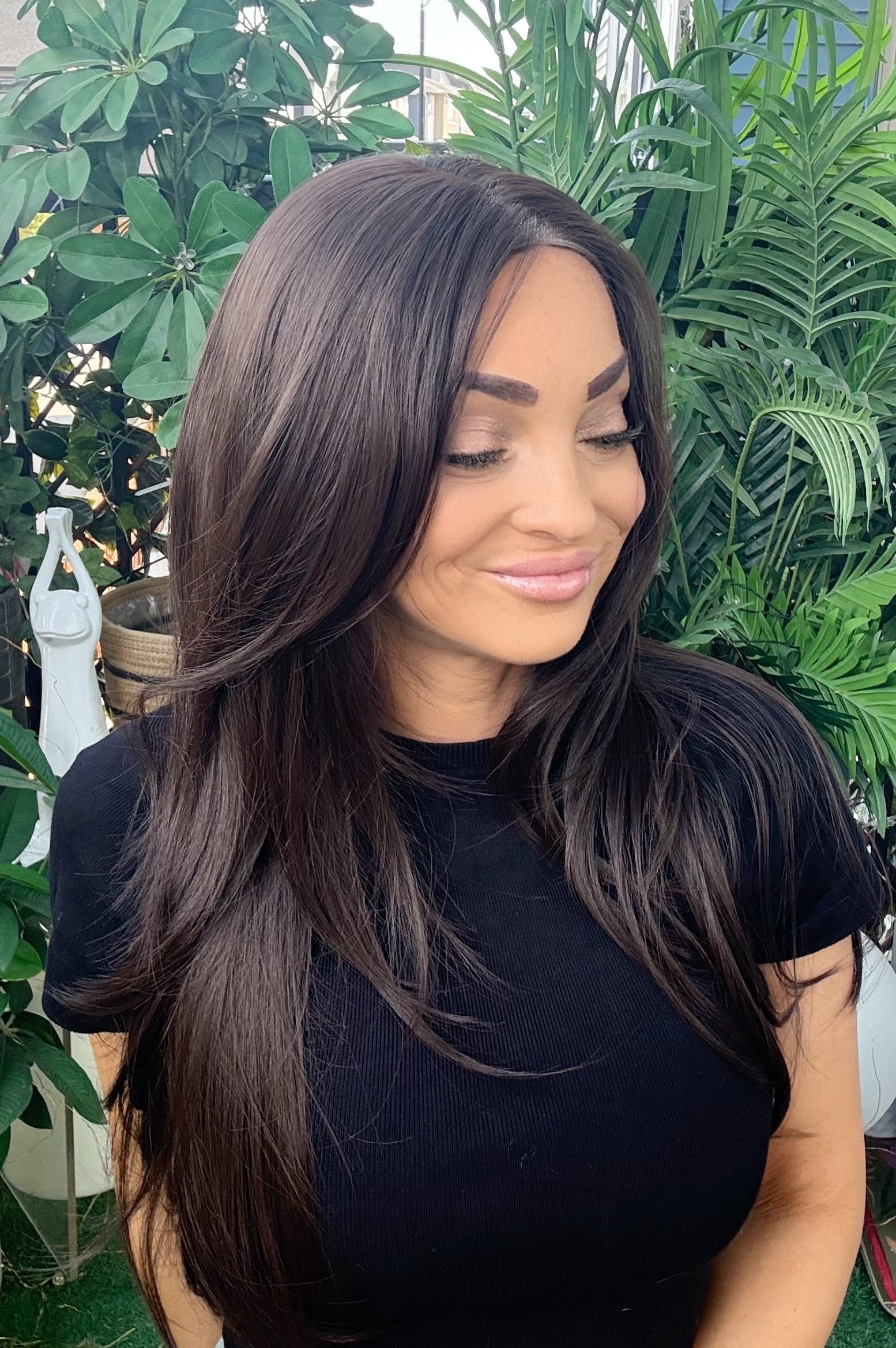 Woman with long dark hair wearing a black top in a garden setting