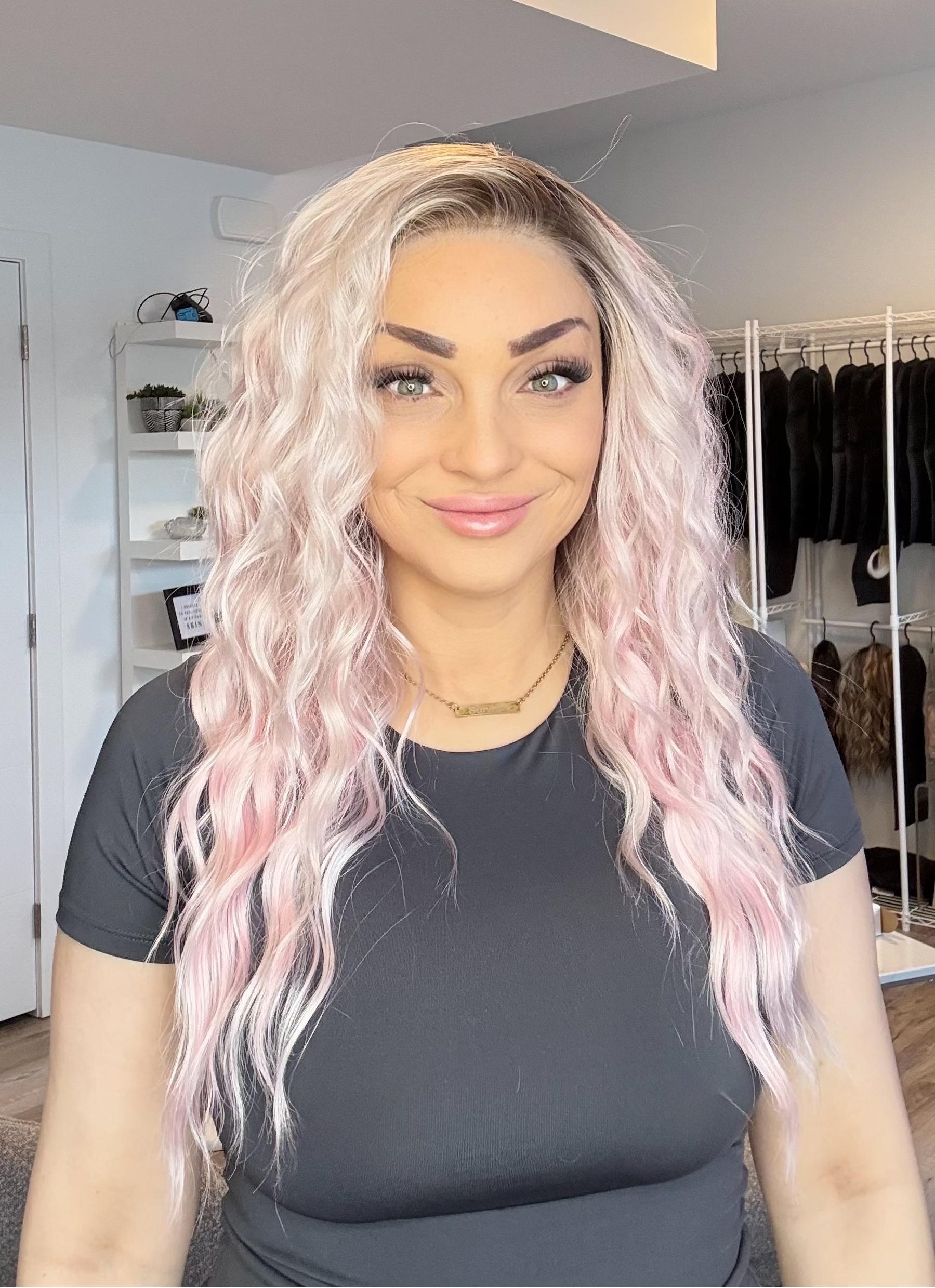Woman with long, wavy hair in a room with clothing racks and shelves.