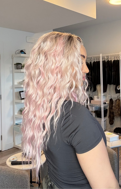 Person with long, wavy hair in a room with a mirror and clothing rack.
