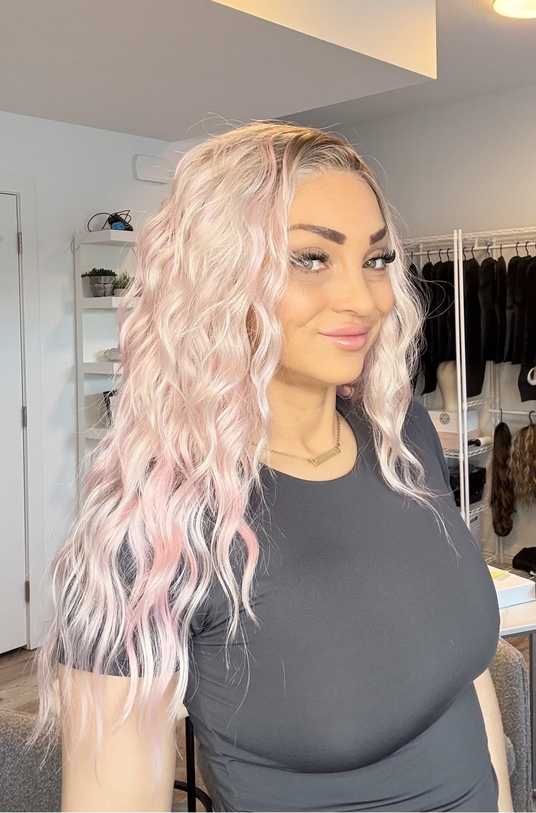 Woman with pink hair in a room with clothing racks and shelves.