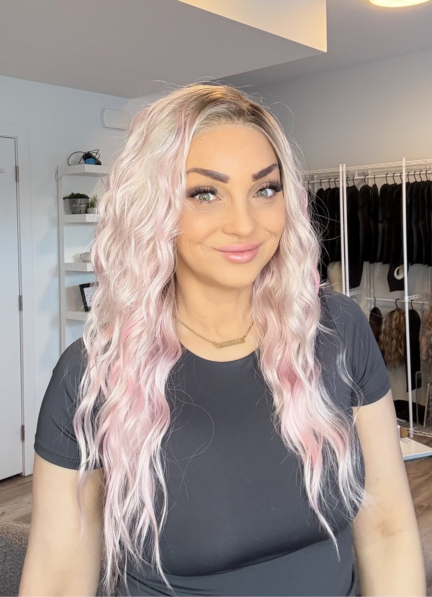 Woman with pink hair in a room with clothing racks and shelves.