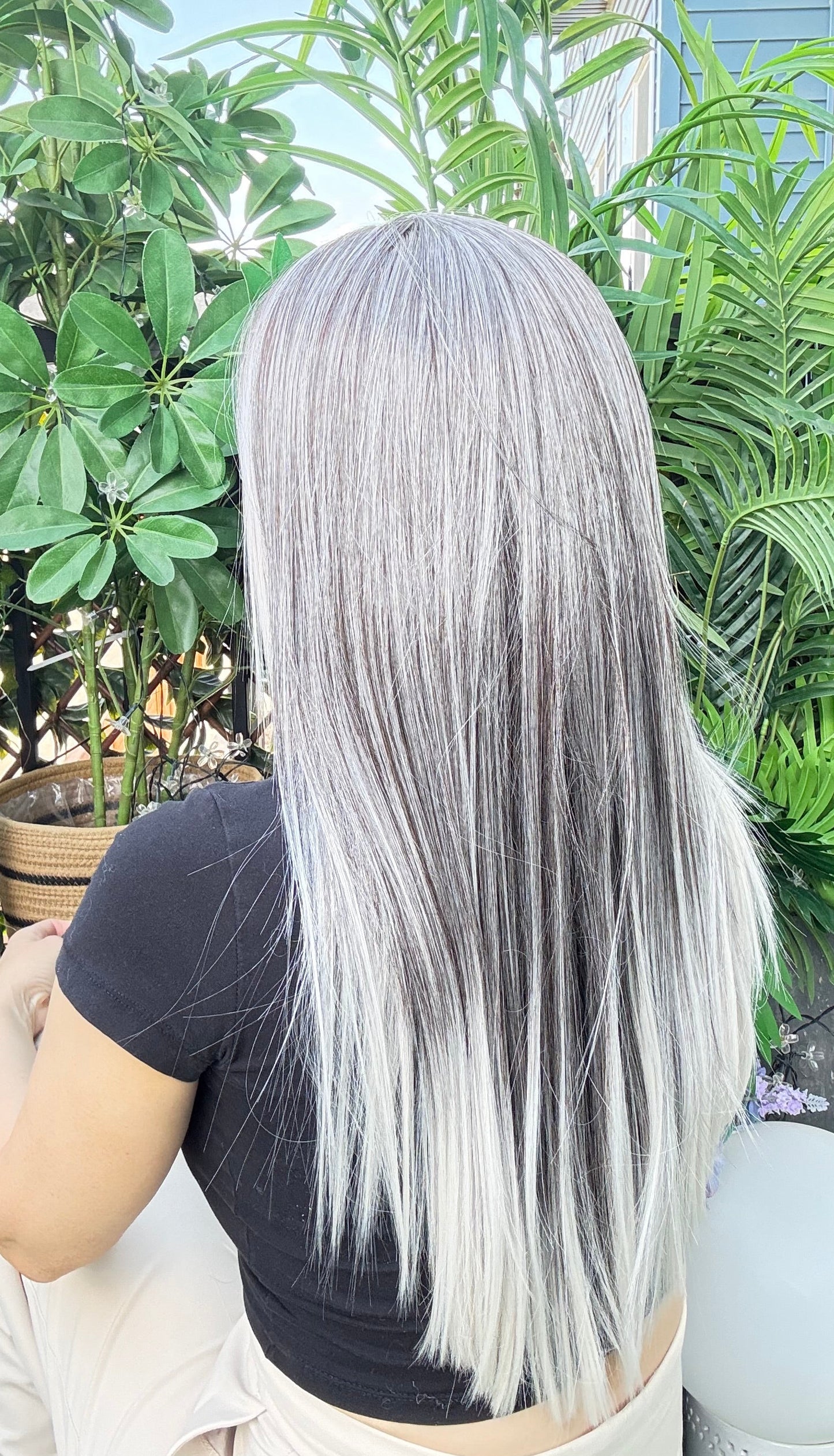 Person with long gray hair sitting outdoors surrounded by greenery
