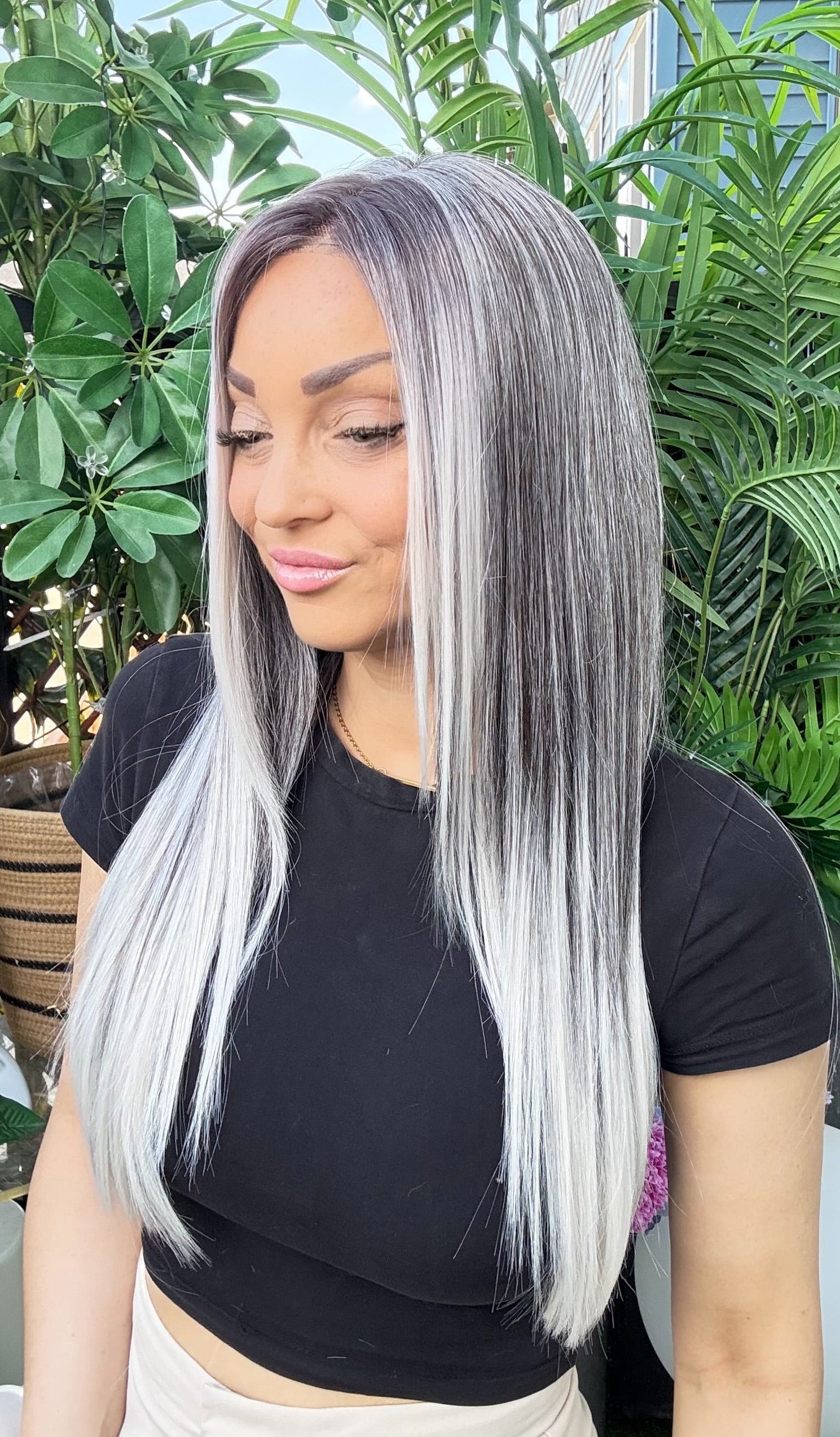 Woman with long silver hair standing outdoors with greenery in the background