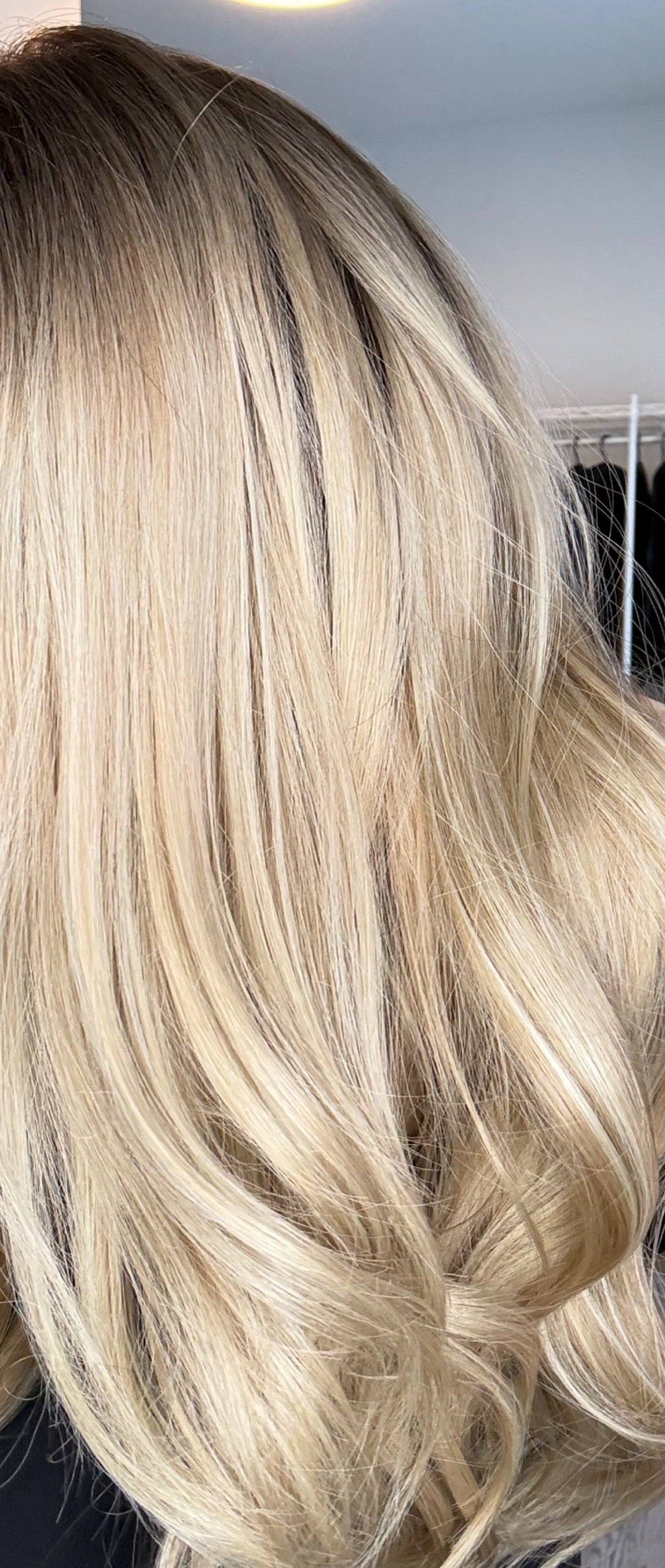 Woman with long, wavy blonde hair in a room with a coat rack and plant.