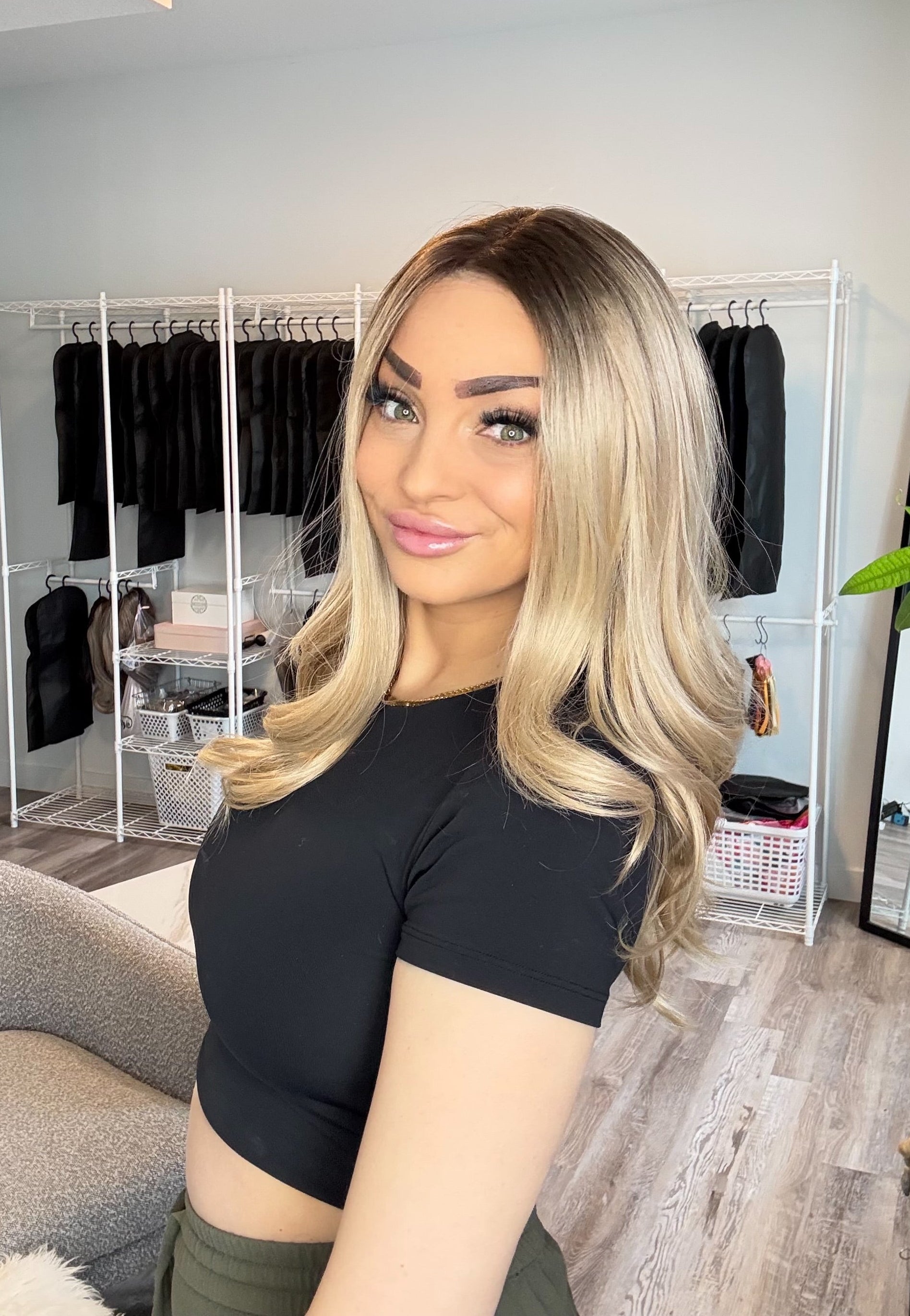 Woman with blonde hair and a black top in a room with clothing racks and decor.