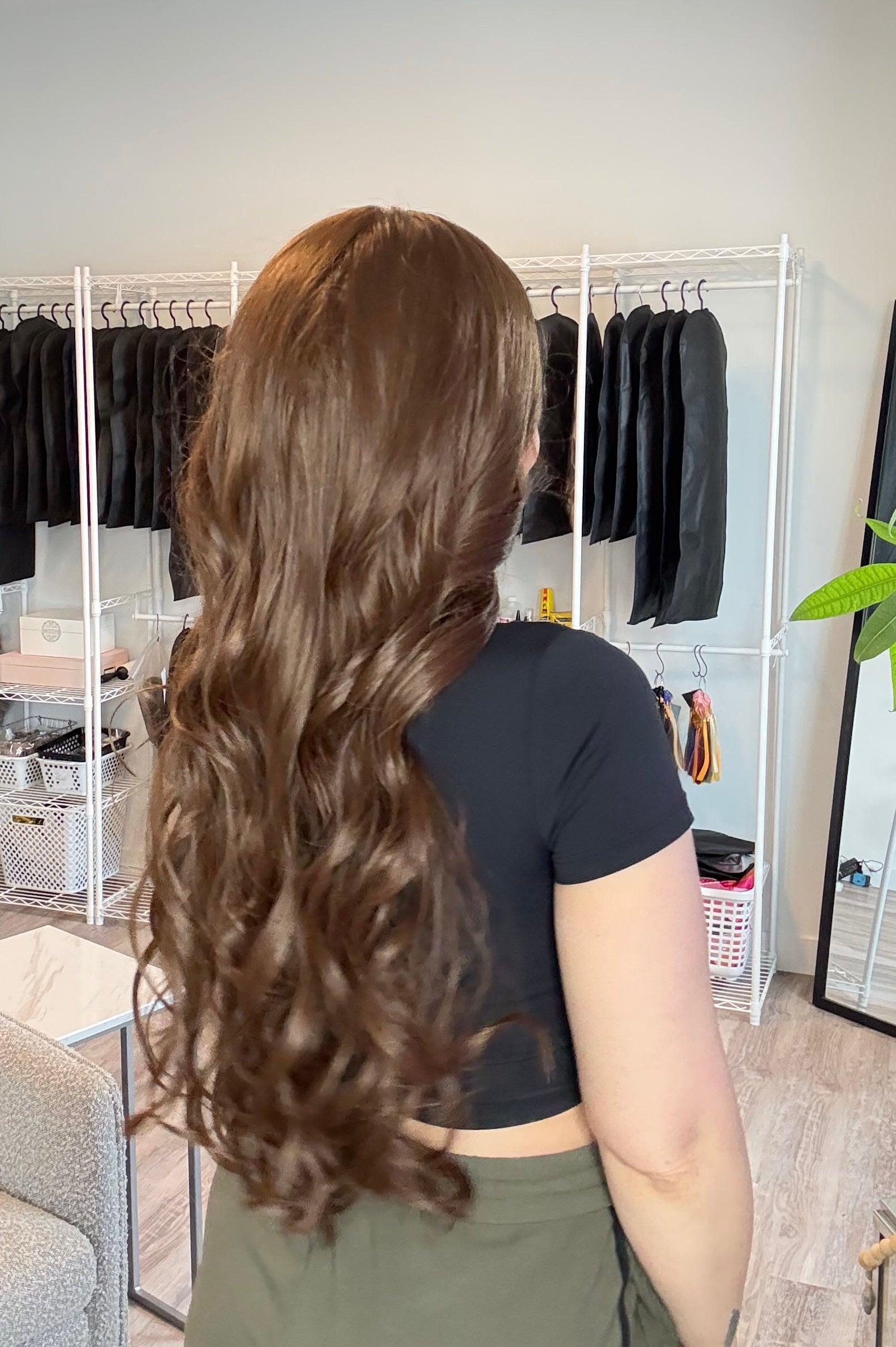 Person with long, wavy hair in a salon setting with hair products on a shelf.