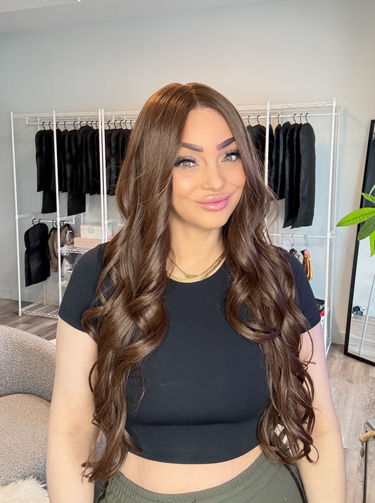 Woman with long, wavy hair in a room with clothing racks and decor.