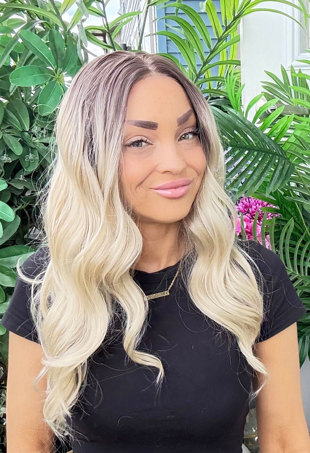 Woman with long blonde hair standing in front of green plants