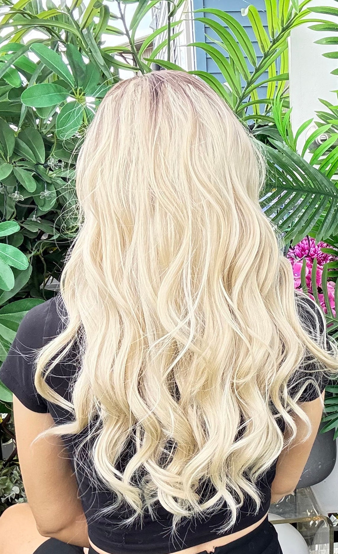 Person with long, wavy blonde hair sitting outdoors with greenery around