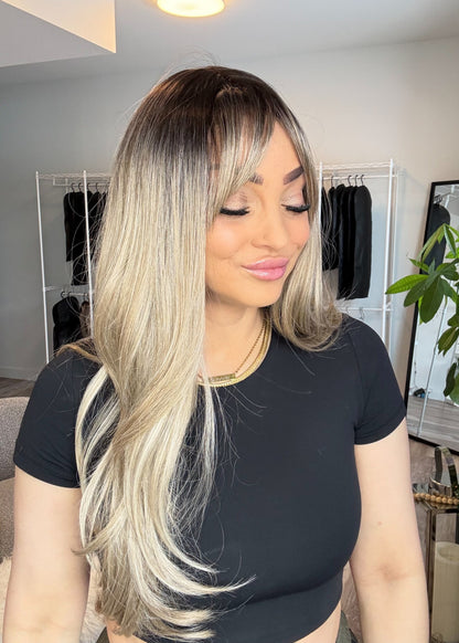 Woman with long, styled hair in a room with clothing racks and a plant.