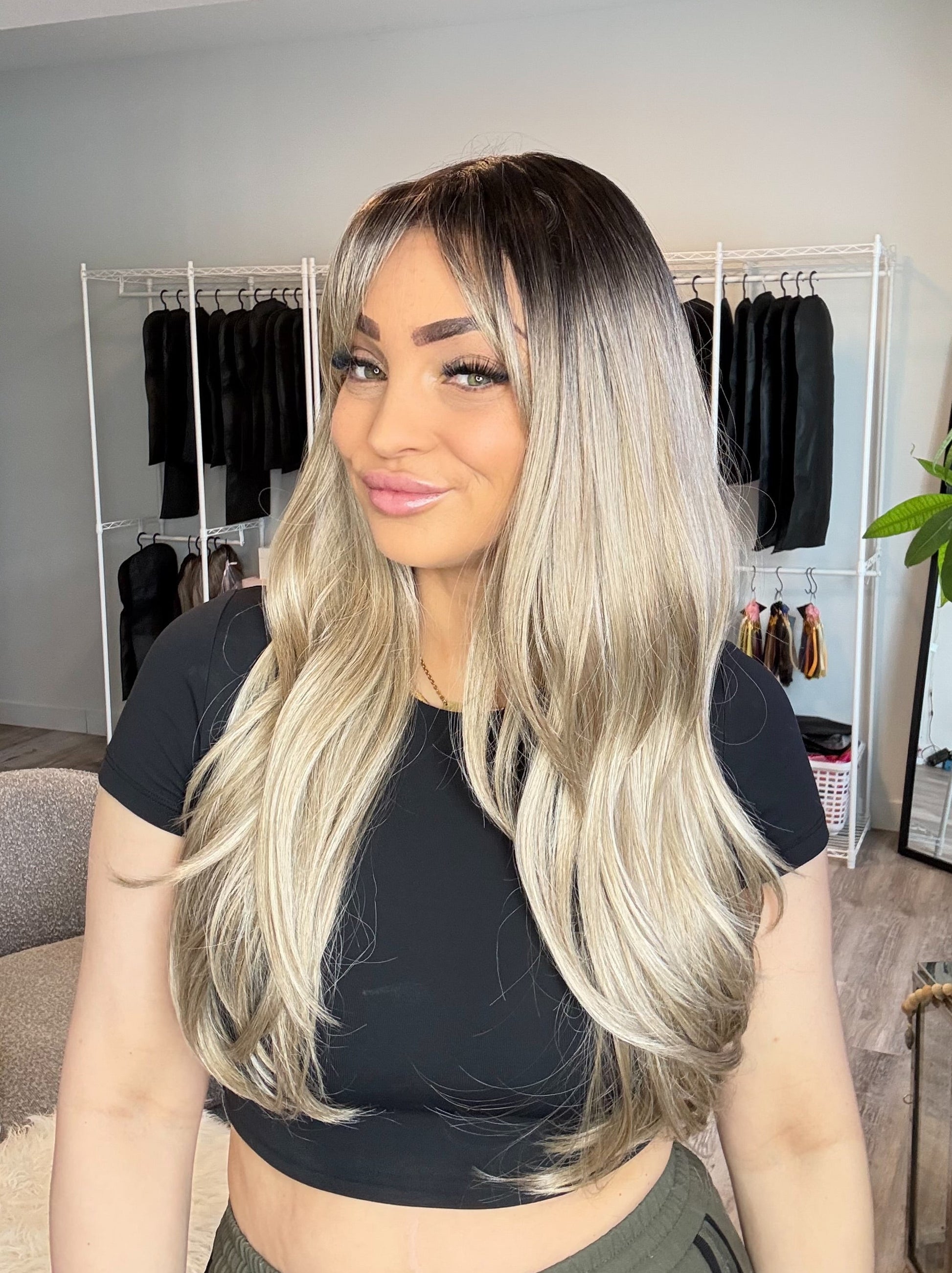 Woman with long blonde hair in a room with clothing racks and a plant.