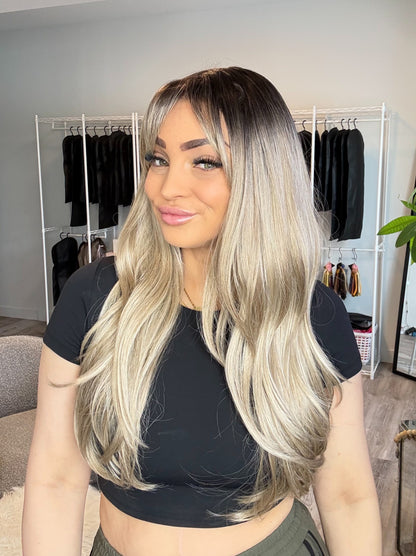 Woman with long blonde hair in a room with clothing racks and a plant.