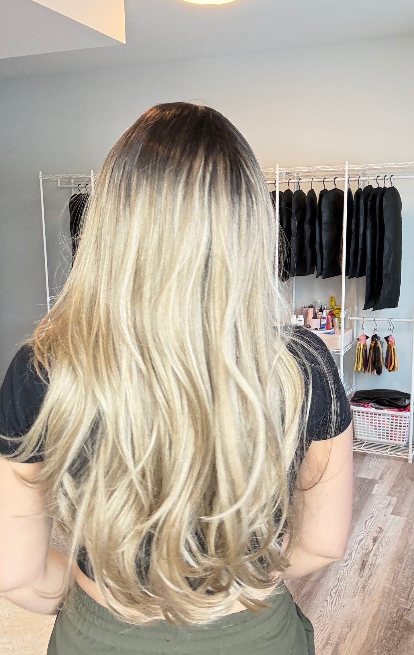 Person with long blonde hair in a salon setting with hair extensions displayed.