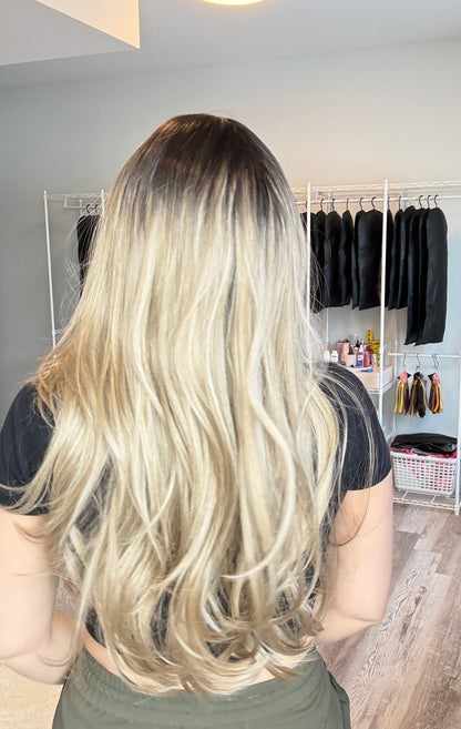 Person with long blonde hair in a salon setting with hair extensions displayed.