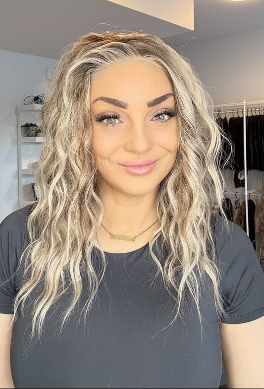 Woman with blonde hair and gray shirt in a room with shelves and a mirror.