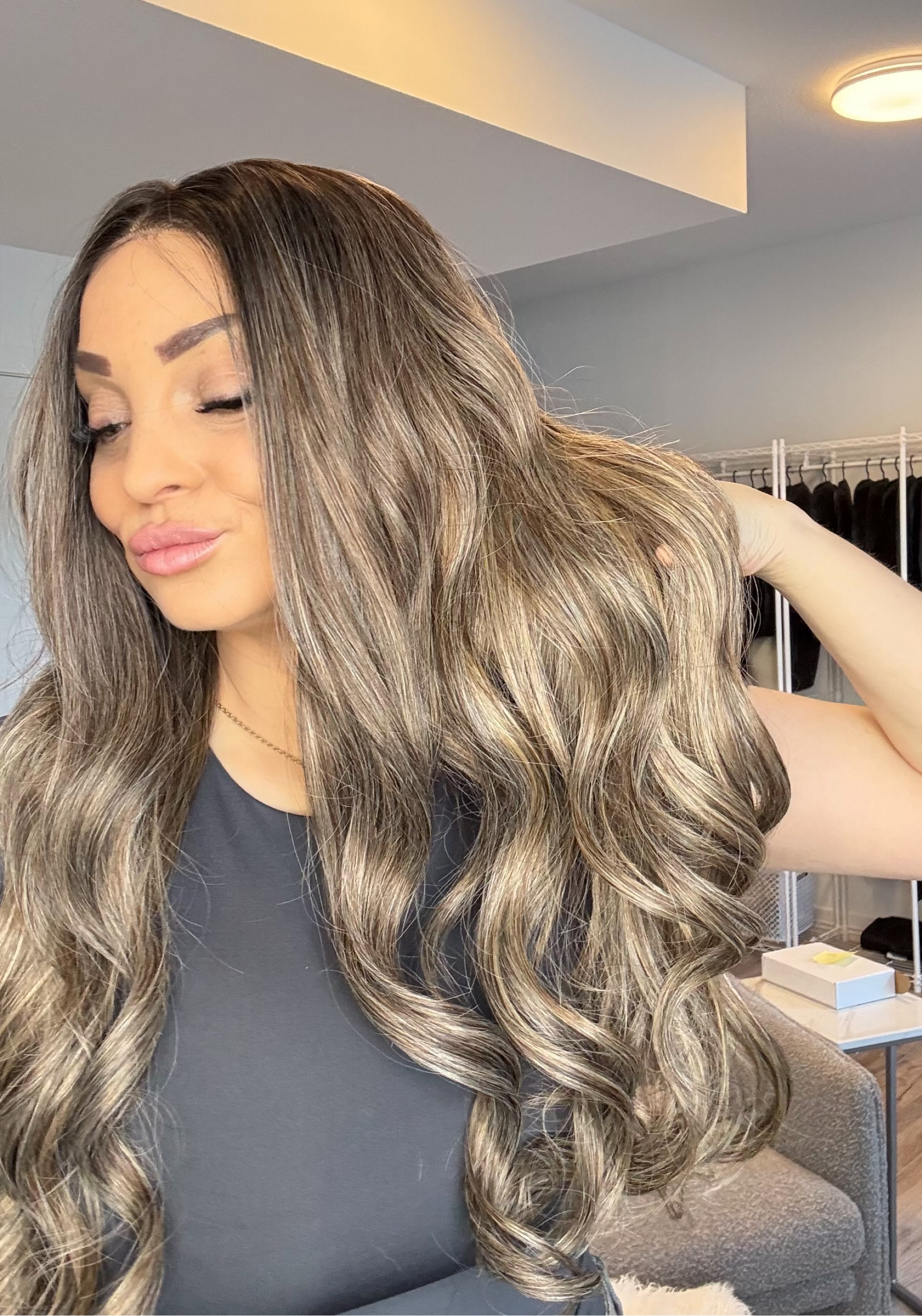 Woman with long, wavy hair in a room with clothing racks.