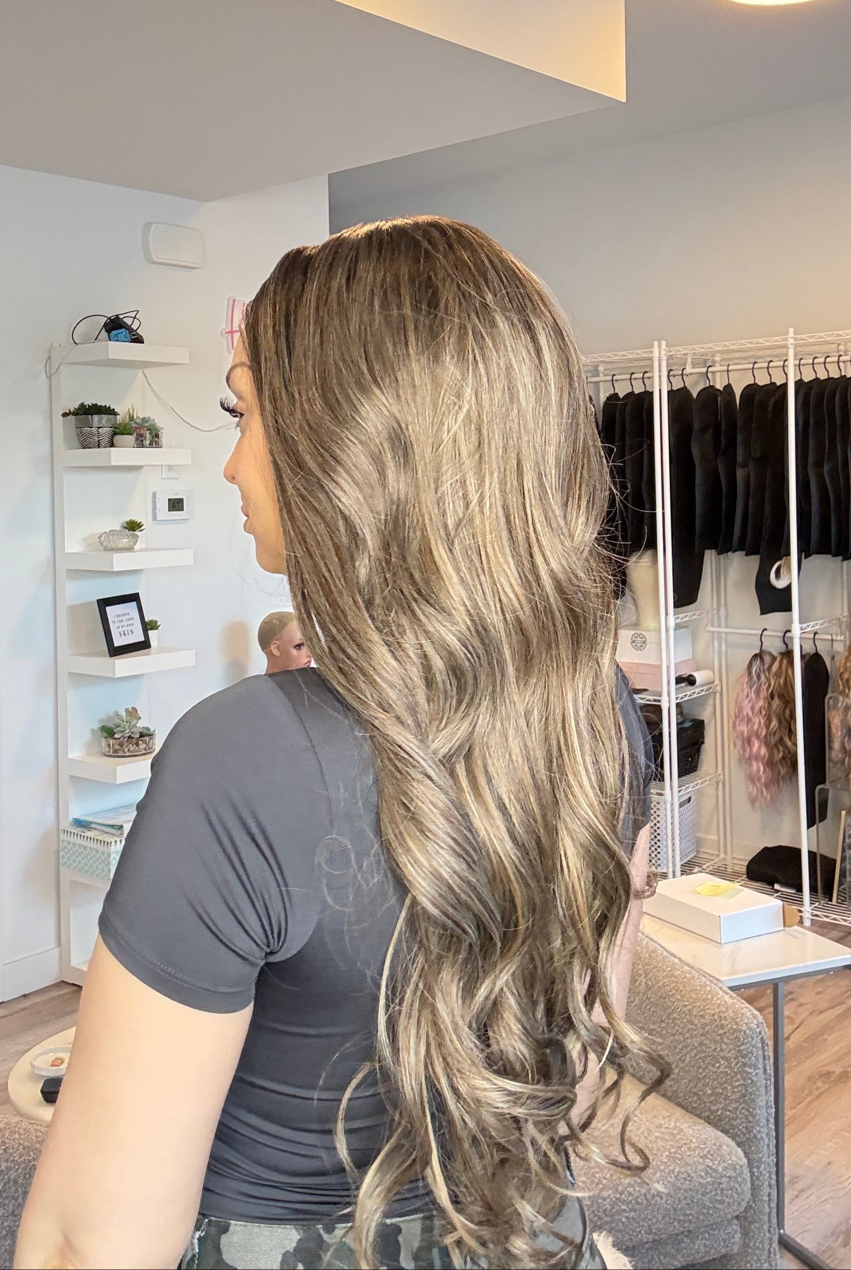 Person with long blonde hair looking into a mirror in a store setting.