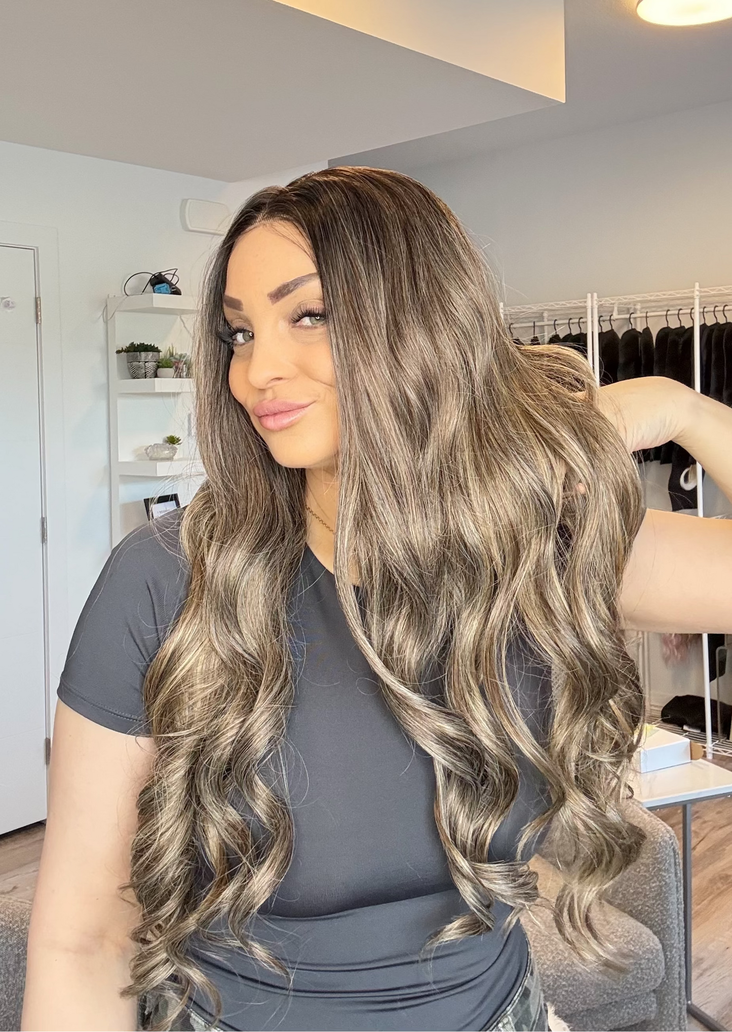 Woman with long, wavy hair in a room with clothing racks and shelves.