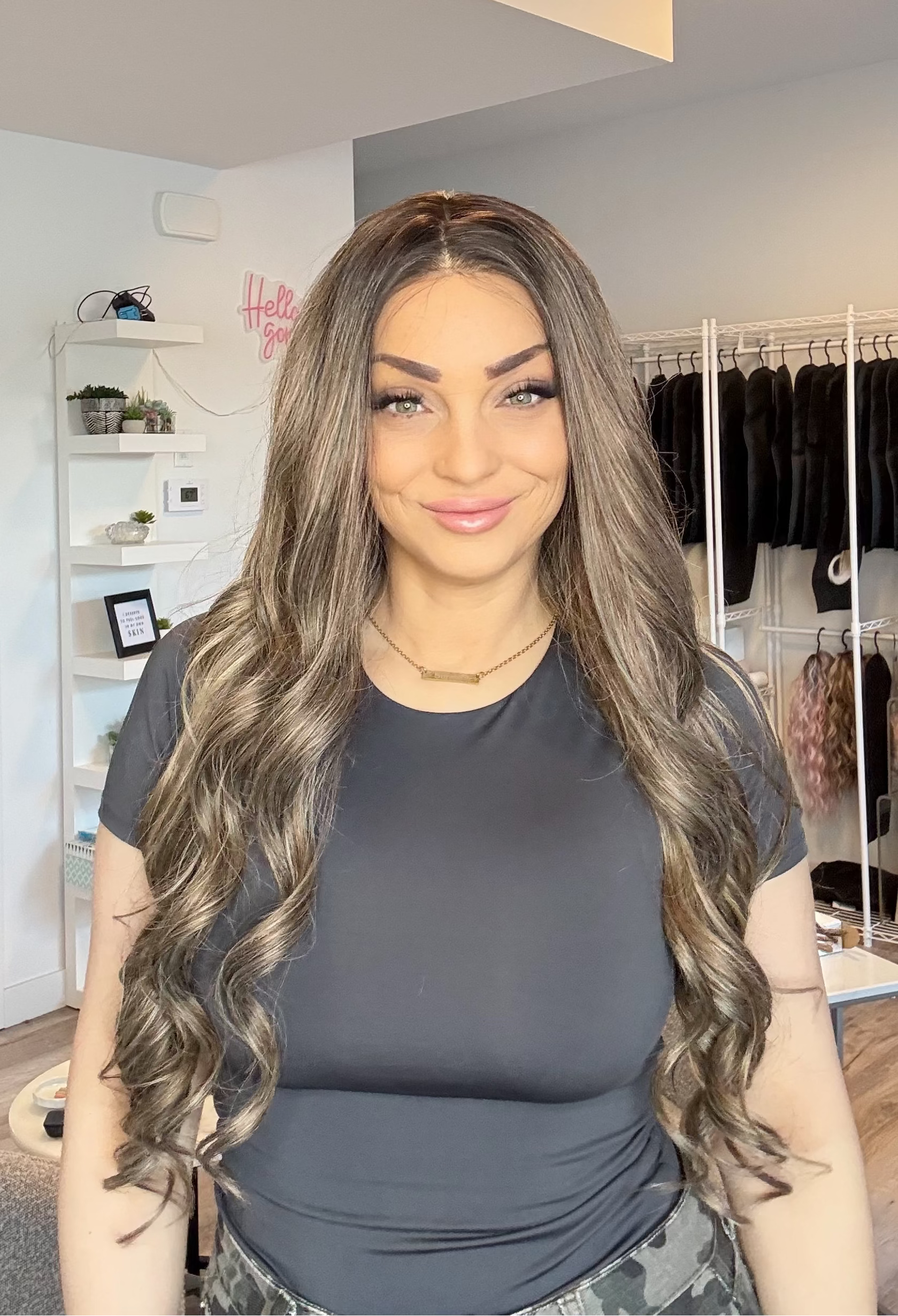 Woman with long, wavy hair standing in a room with clothing racks and shelves.