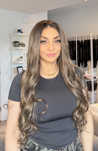 Woman with long, wavy hair in a room with clothing racks and shelves.