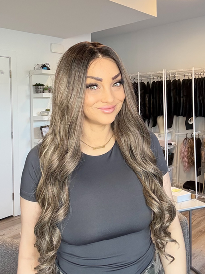 Woman with long, wavy hair standing in a room with clothing racks in the background.