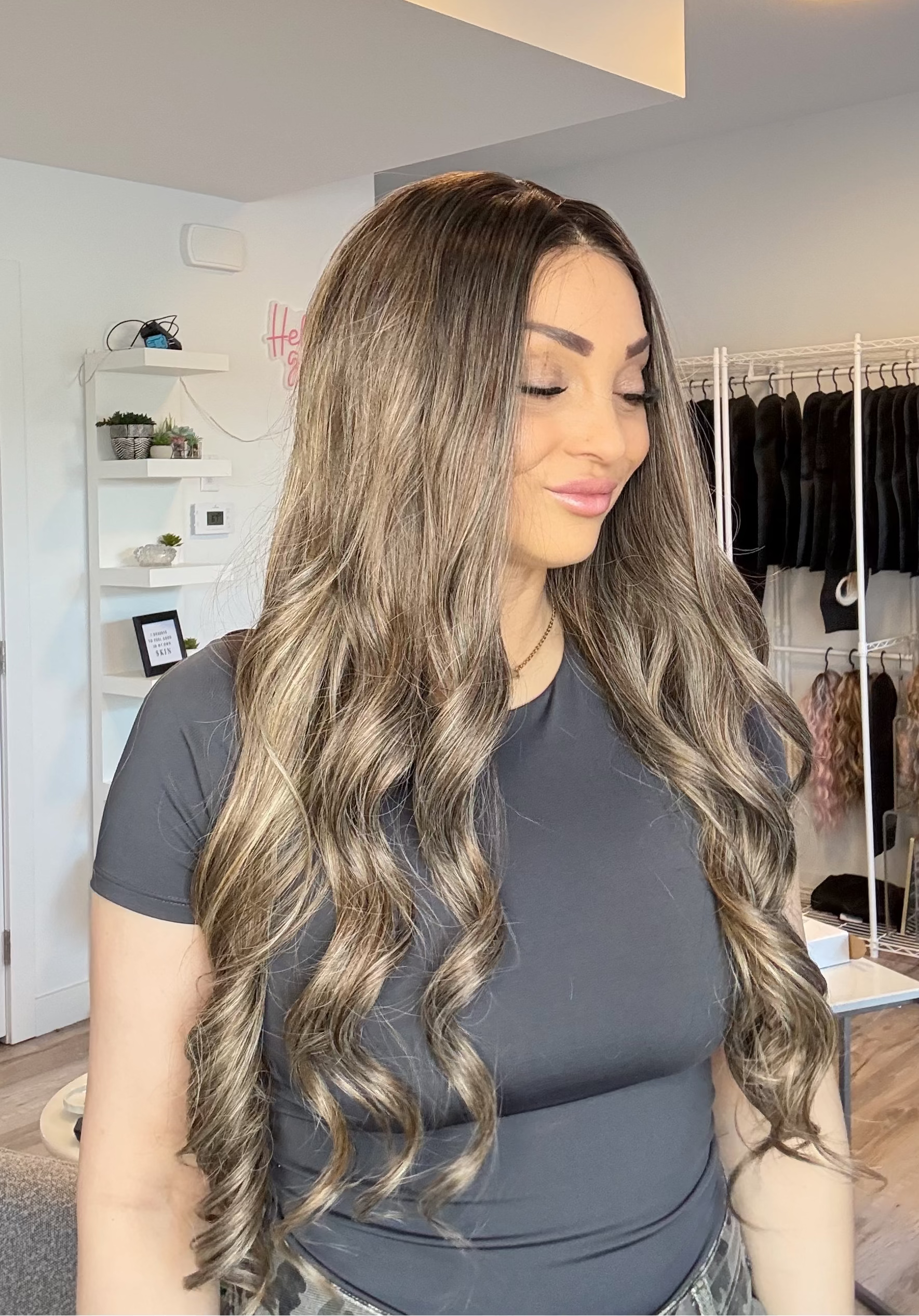 Woman with long, wavy hair in a room with clothing racks and shelves.