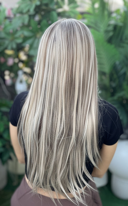 Person with long blonde hair sitting outdoors surrounded by greenery and flowers.