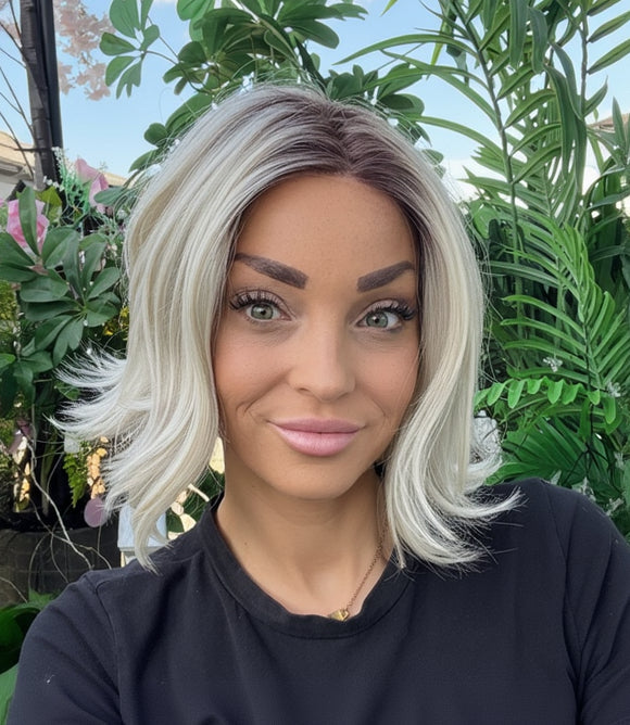 Woman with blonde hair and black shirt sitting outdoors with greenery in the background