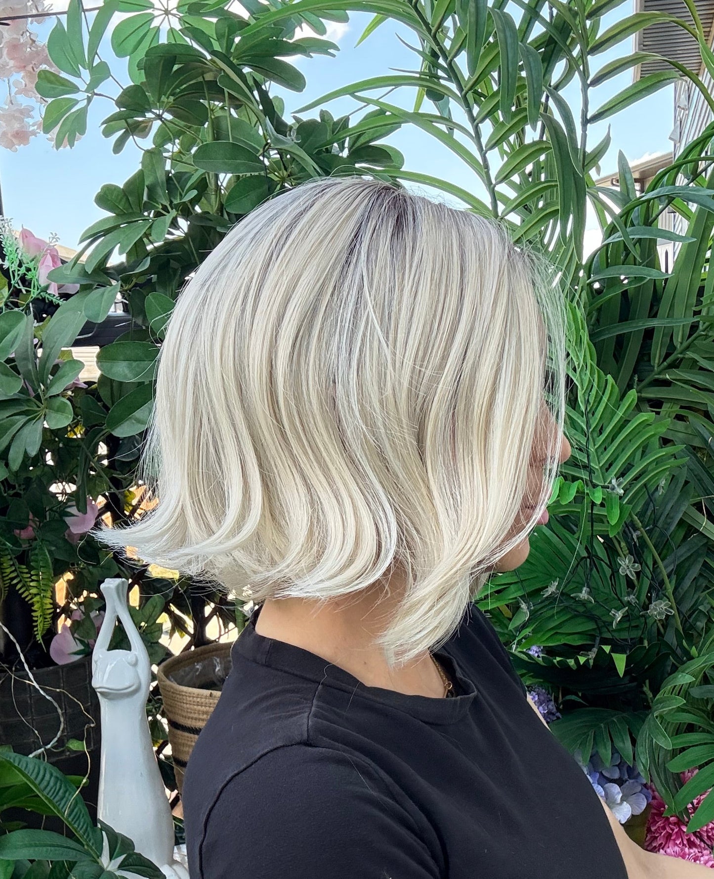 Person with platinum blonde hair standing among green plants