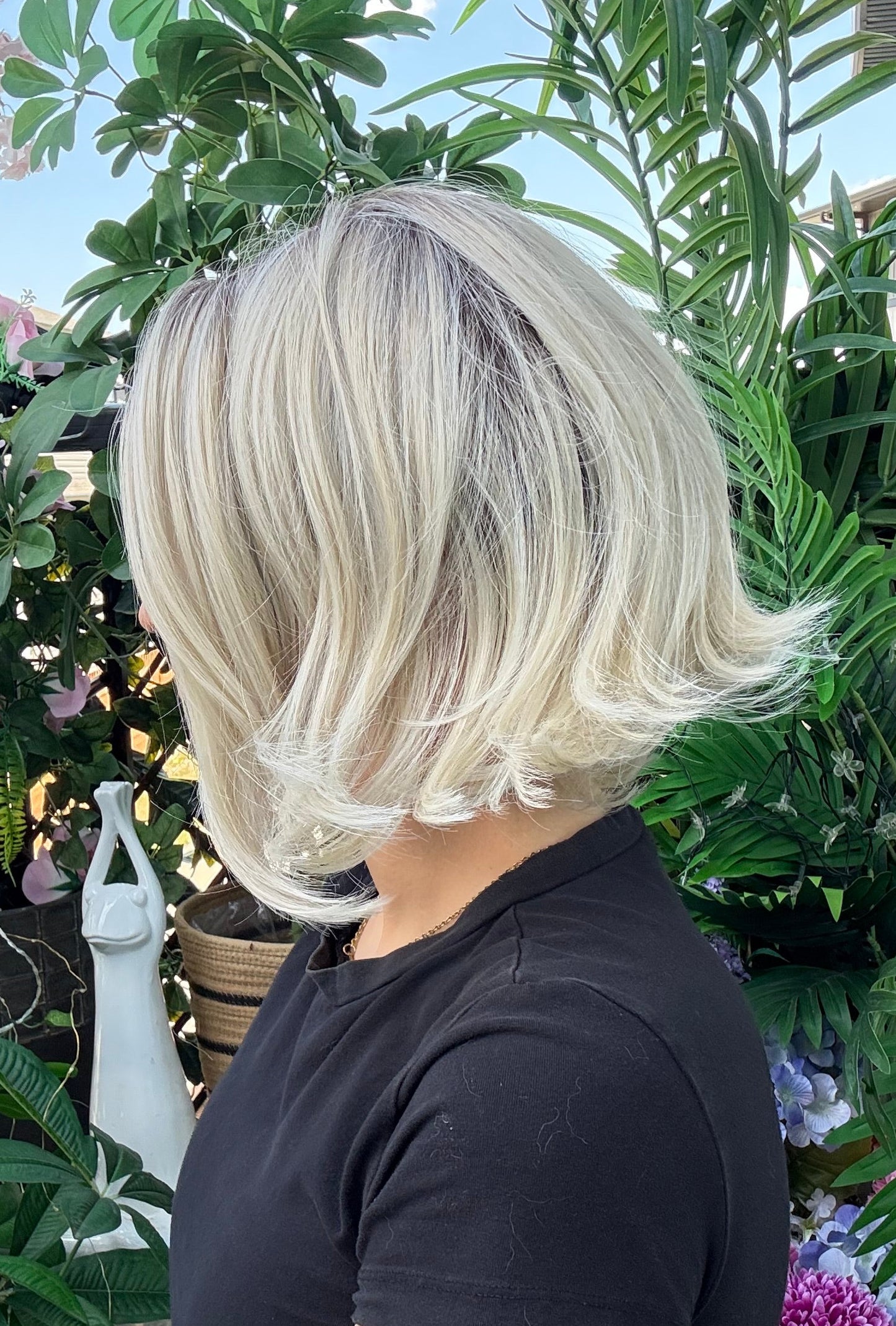 Person holding a blonde wig outdoors with greenery in the background