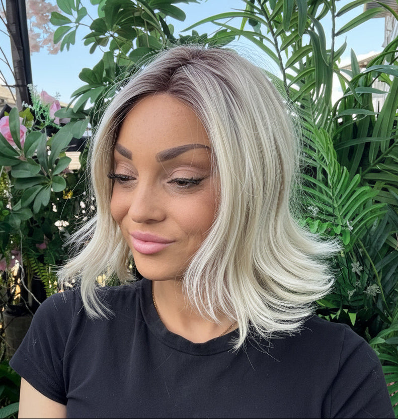 Woman with blonde hair and a black shirt standing in front of green plants