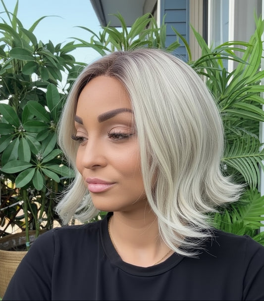 Person with a stylish haircut standing outdoors with plants in the background