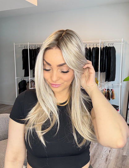 Woman with long blonde hair adjusting it in a room with clothing racks.