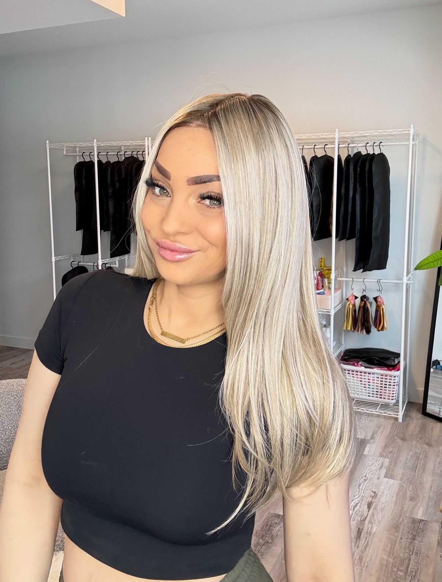 Woman with long blonde hair in a room with clothing racks and a plant.