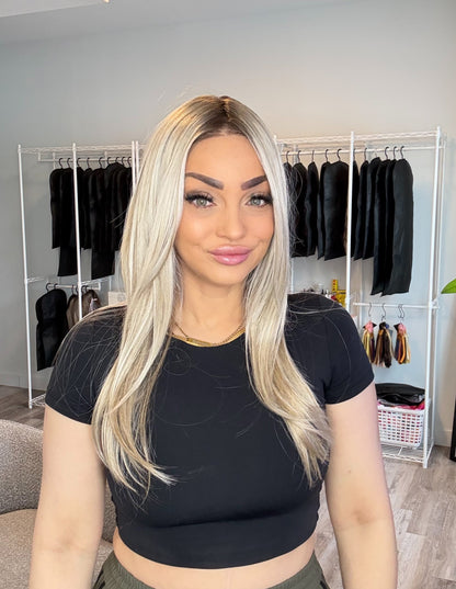 Woman in a black crop top and green pants standing in a room with clothing racks in the background.
