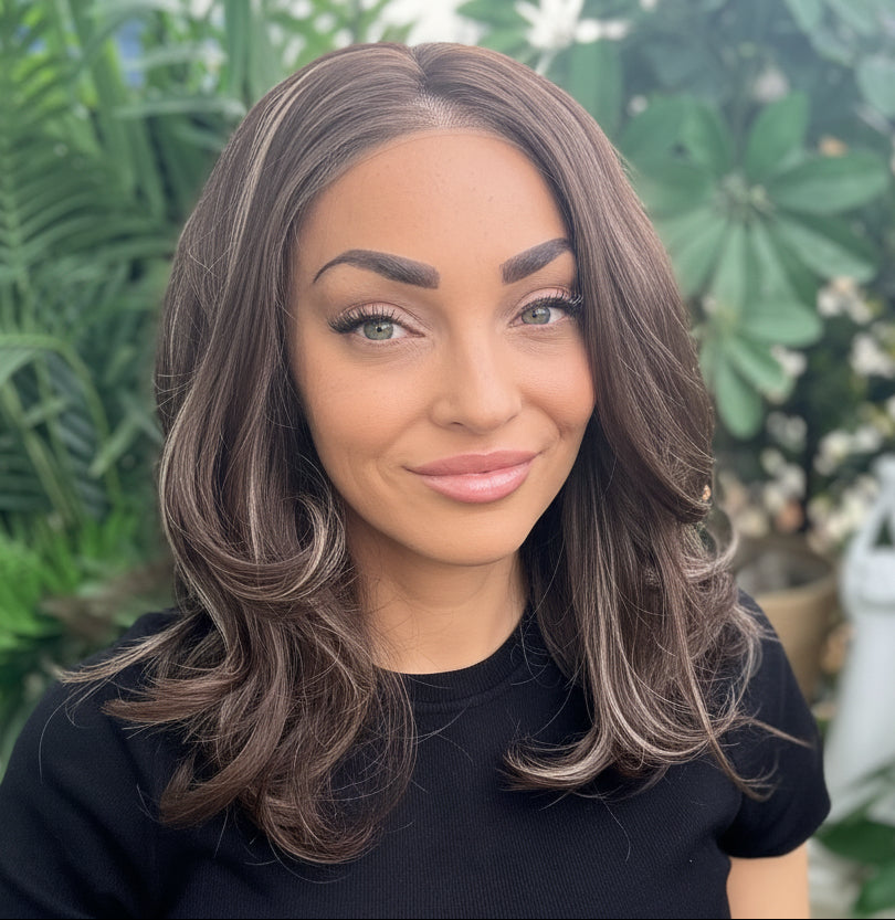 Woman with long brown hair sitting outdoors surrounded by greenery