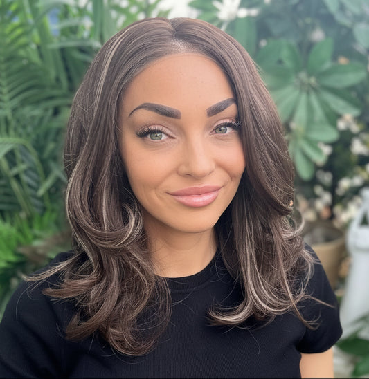 Woman with long brown hair sitting outdoors surrounded by greenery